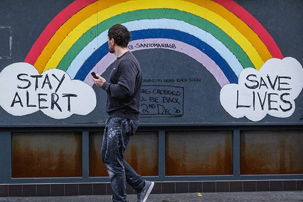 homem a andar a olhar para uma parede com um arco iris pintado
