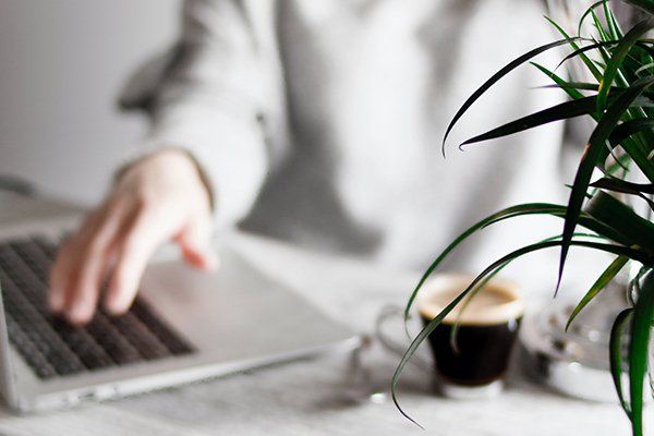 Pessoa a trabalhar no computador com um café e uma planta ao lado representando a parte de emprego