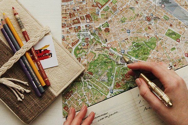 Pessoa a planear a sua viagem com um mapa, um caderno e alguns lápis na mesa
